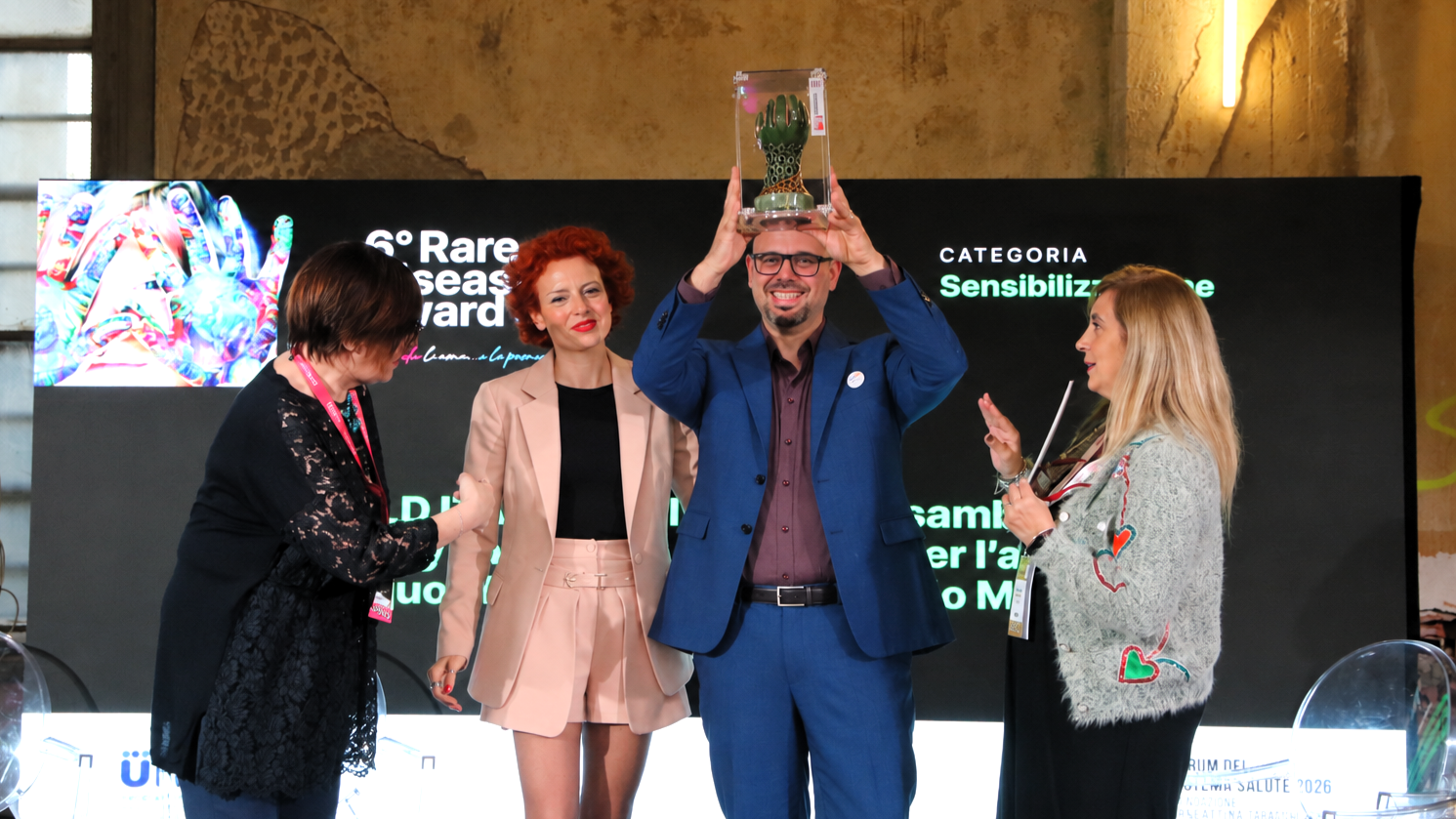 Guido De Barros solleva il trofeo del Rare Diseases Award, accanto agli altri partecipanti sul palco.