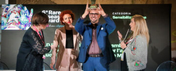 Guido De Barros solleva il trofeo del Rare Diseases Award 2026 sul palco, accanto a Caterina Ceccuti e alle altre partecipanti.