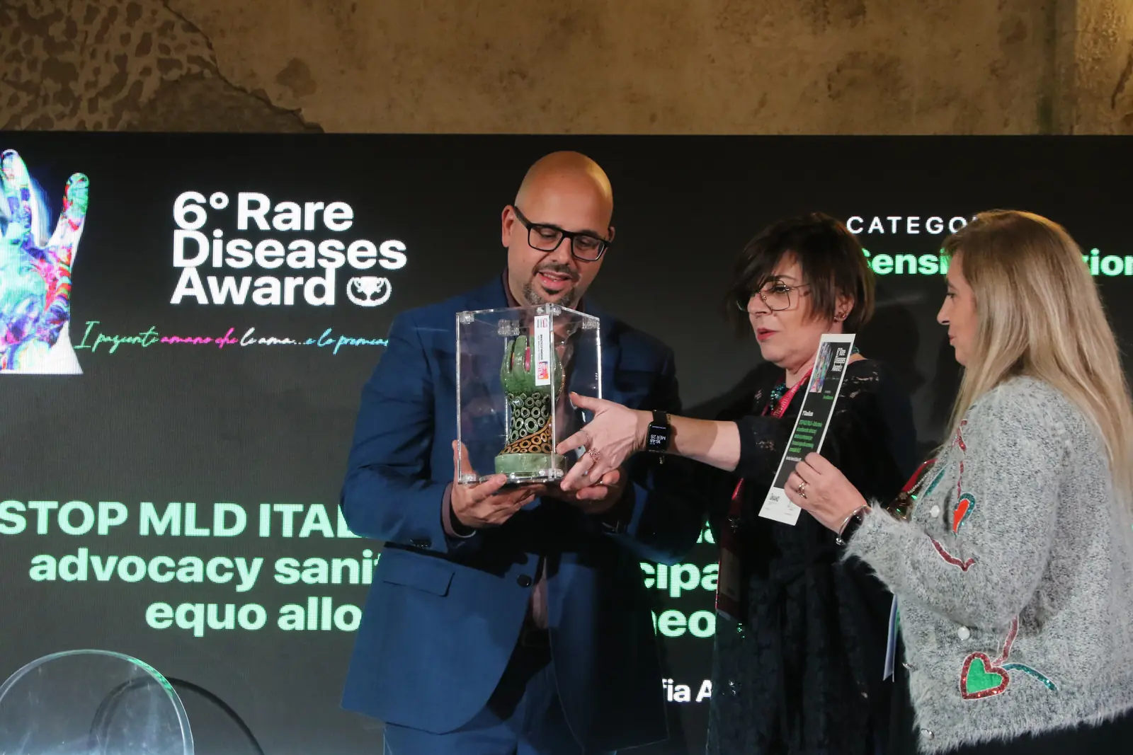Guido De Barros riceve il trofeo sul palco, davanti allo schermo del Rare Diseases Award.